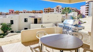 Een balkon met een barbecue en zitgedeelte met uitzicht op een woonwijk.
