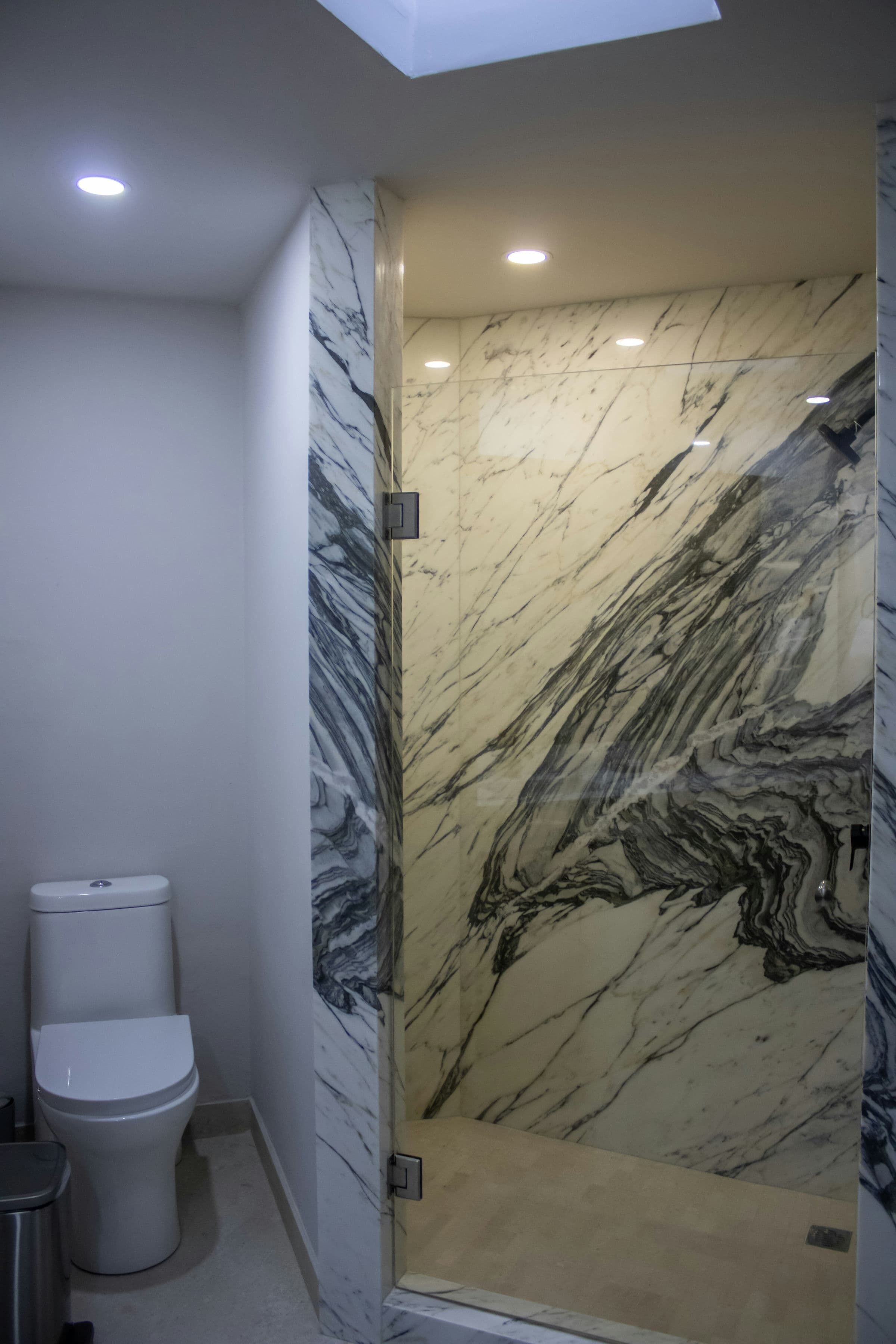A bathroom with a marble wall, a toilet, and a shower enclosure.