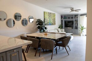 A modern living room with a dining area, a ceiling fan, and a large mirror collection.