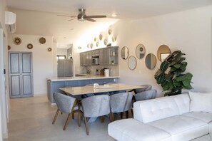 A modern kitchen with grey cabinets, a central island, and a dining area with grey chairs.