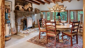 A rustic dining area with a stone fireplace, wooden chairs, and a chandelier.