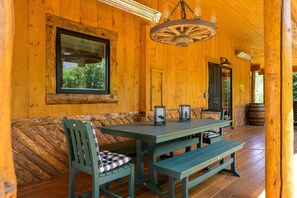 A wooden cabin interior with a wooden table, benches, and a window overlooking greenery.