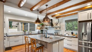 A modern kitchen with a central island, stainless steel appliances, and wooden beams on the ceiling.
