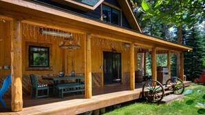 A wooden cabin with a covered porch, a dining table, chairs, and a large wheel.