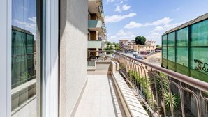 Un balcon donnant sur une rue, un immeuble à la façade verdoyante et un ciel dégagé.