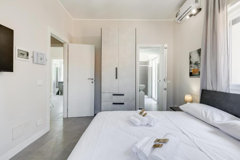 A hotel room with a large bed, a wardrobe, a bedside table with a lamp, and a bathroom visible through an open door.