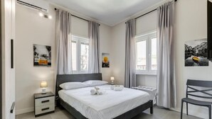Une chambre à coucher moderne avec un grand lit, deux tables de chevet, une chaise et des œuvres d’art accrochées aux murs.