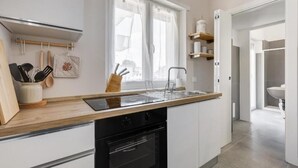 Une cuisine moderne avec un plan de travail en bois, des appareils électroménagers noirs et une fenêtre ornée de rideaux légers.