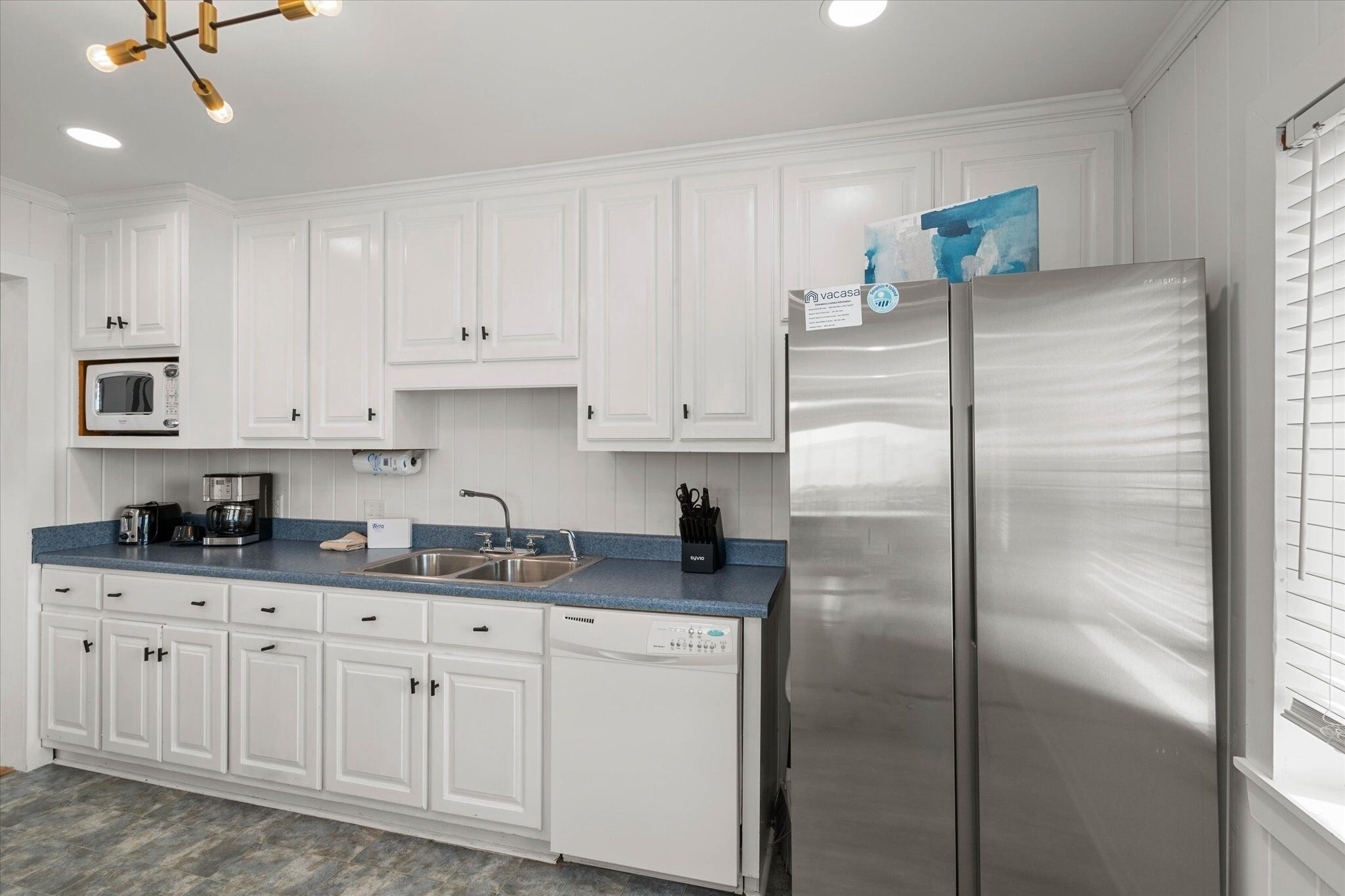 A modern kitchen with white cabinets, a stainless steel refrigerator, a microwave, and a coffee maker.