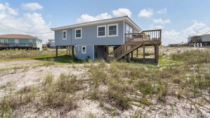 A two-story house with a wooden deck and a small attached structure. - Dauphin Island Escape - 102 Ponchartrain Ct 3 Bedroom Home (Dauphin Island)