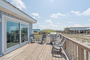 A wooden deck with outdoor seating and a grill, overlooking a beach and other buildings. - Dauphin Island Escape - 102 Ponchartrain Ct 3 Bedroom Home (Dauphin Island)