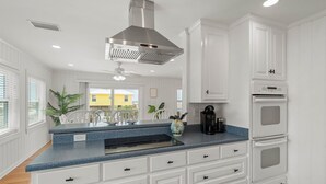 A kitchen with white cabinets, a blue countertop, a stainless steel range hood, and a built-in oven. - Dauphin Island Escape - 102 Ponchartrain Ct 3 Bedroom Home (Dauphin Island)