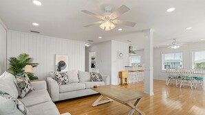 A spacious living room with a sofa, coffee table, and dining area with chairs. - Dauphin Island Escape - 102 Ponchartrain Ct 3 Bedroom Home (Dauphin Island)