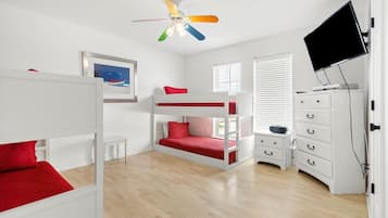A room with bunk beds, a ceiling fan, a TV, and a dresser.