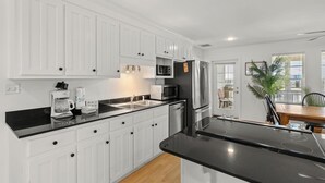 Eine moderne Küche mit weißen Schränken, schwarzen Arbeitsplatten, Edelstahlgeräten und einem Essbereich mit Holztisch und Stühlen.