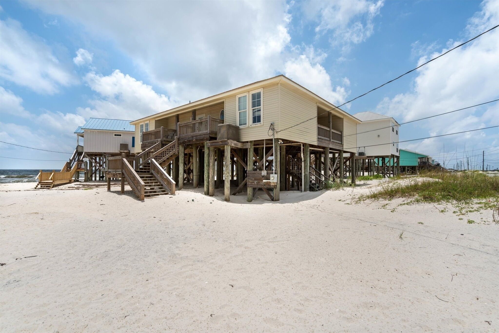 A beachfront house with a wooden deck, a staircase leading to a balcony, and a small porch area.