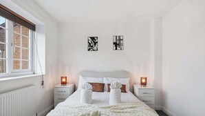 Une chambre à coucher comprenant un lit, deux tables de chevet, une fenêtre et deux œuvres d’art mural.