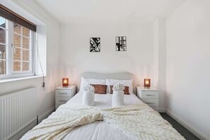 Une chambre à coucher comprenant un lit, deux tables de chevet, une fenêtre et deux œuvres d’art mural.