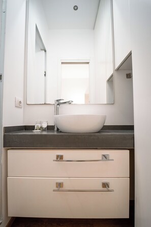 Ein modernes Badezimmer mit einem weißen Waschbecken, einem großen Spiegel und zwei Schubladen.