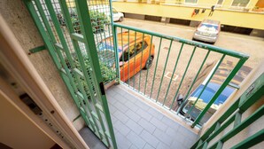 Udsigt fra en balkon over en gade med parkerede biler og en bygning med gule vægge.