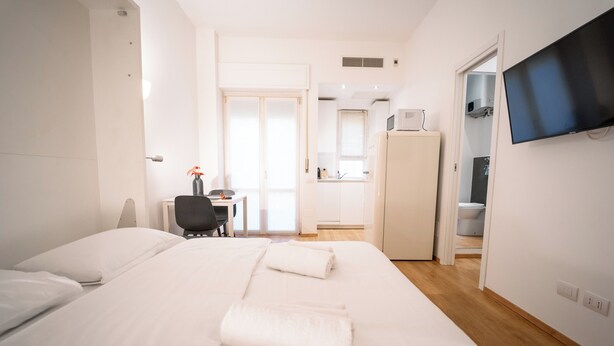 Et hotelværelse med seng, skrivebord, stol, fjernsyn og tekøkken.