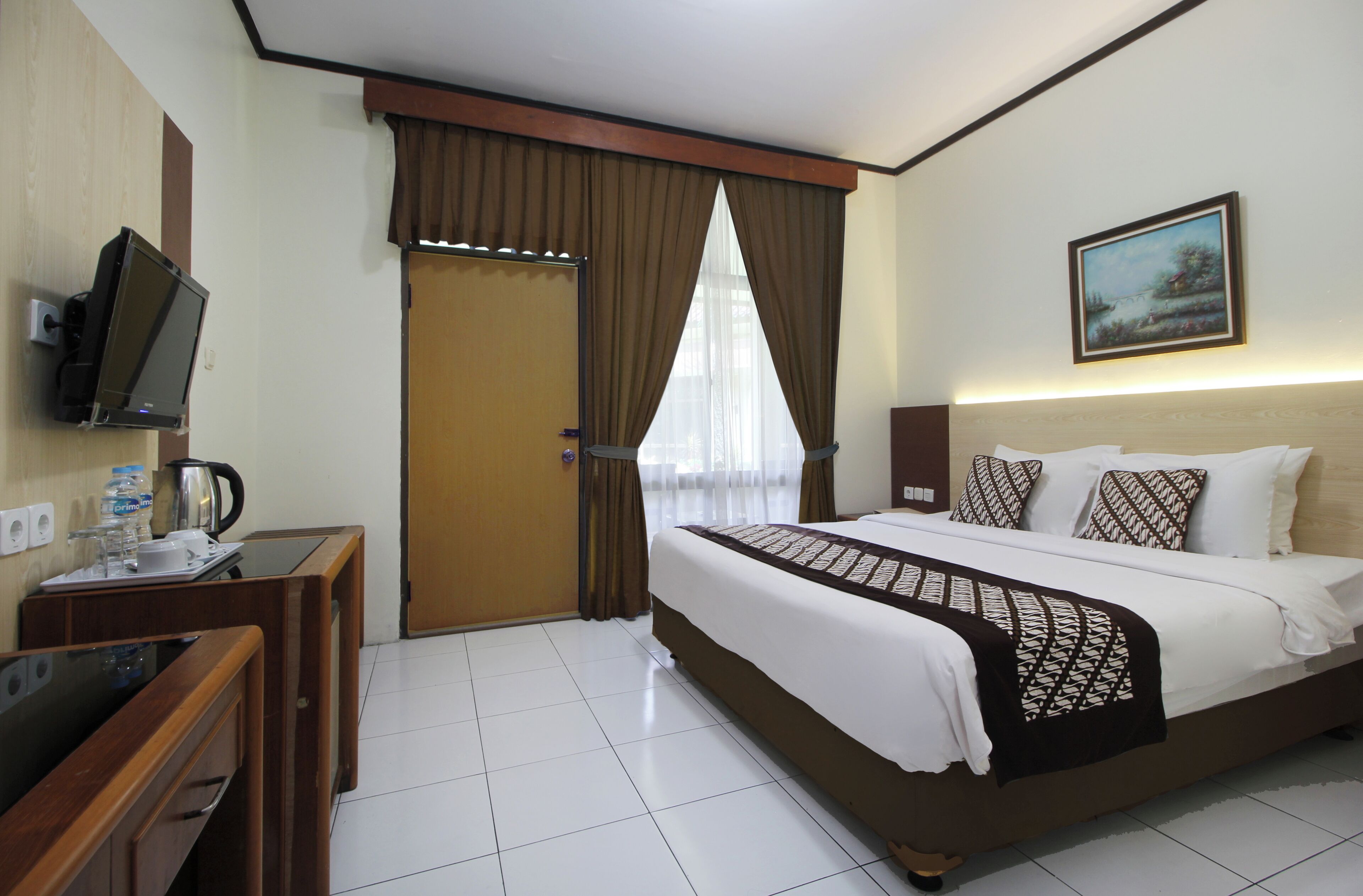 A hotel room with a bed, a desk with a television, a painting on the wall, and a window with curtains.