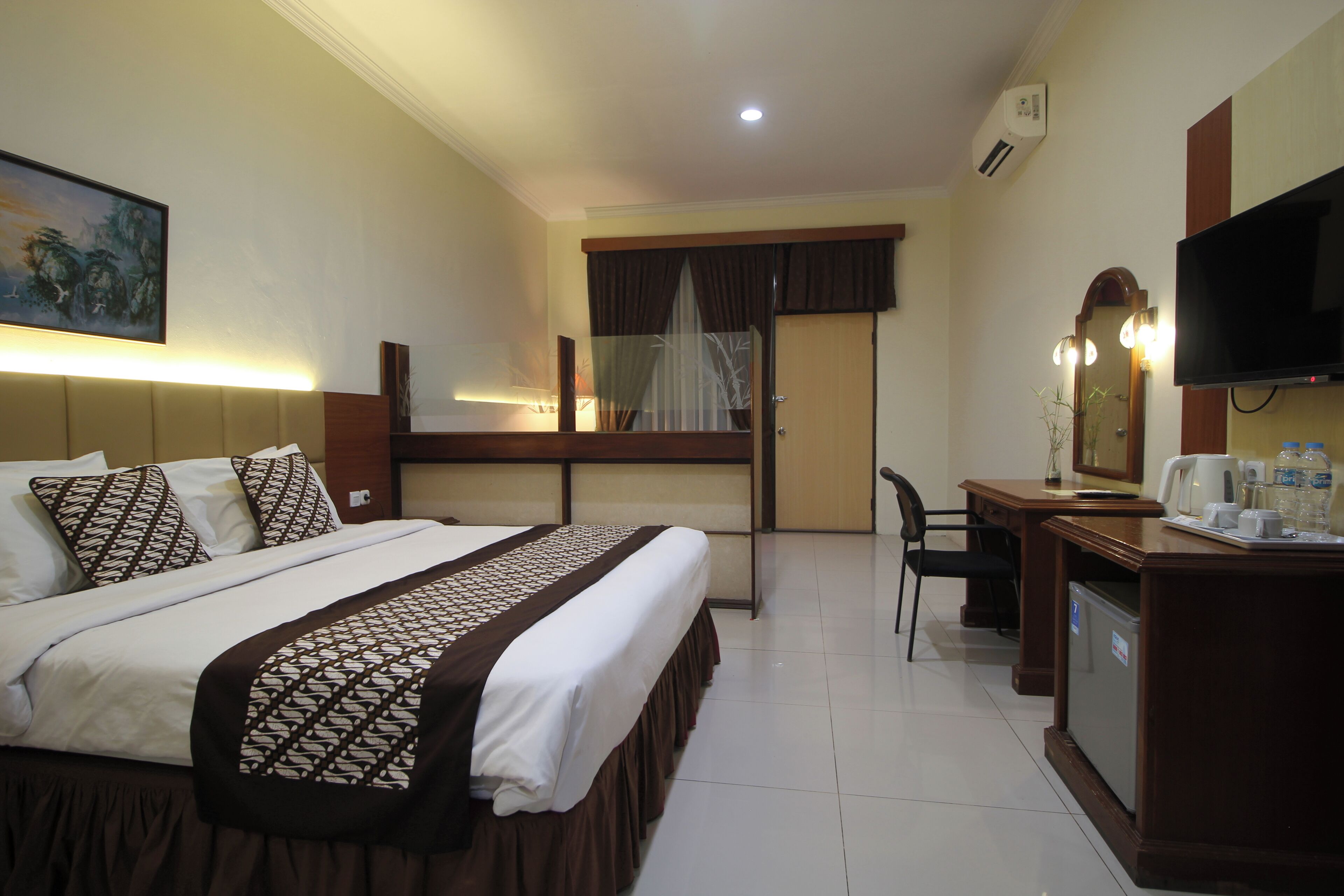 A hotel room with a bed, desk, chair, TV, and a small refrigerator.