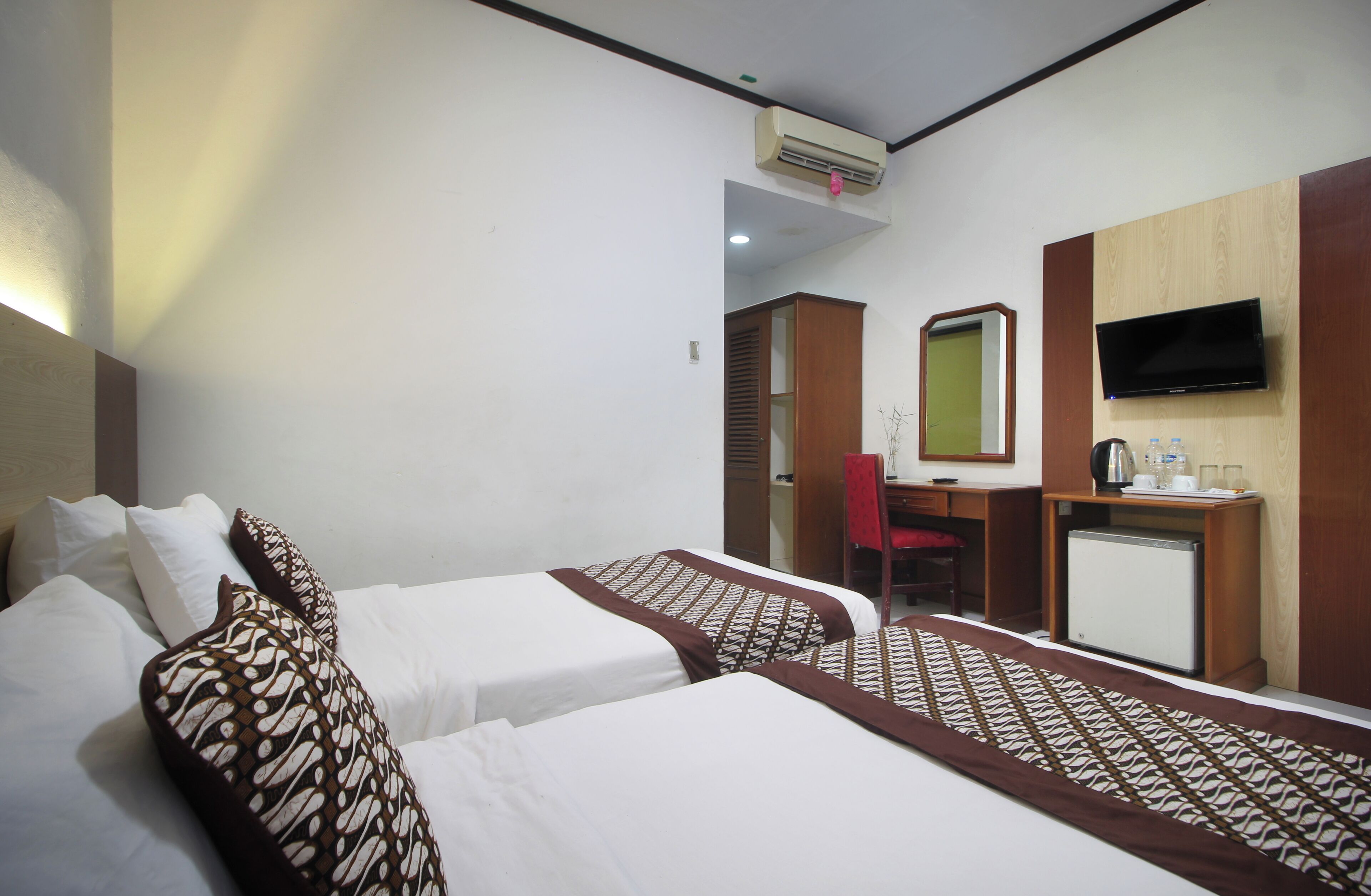 A hotel room with two beds, a desk, a chair, a television, and a small refrigerator.
