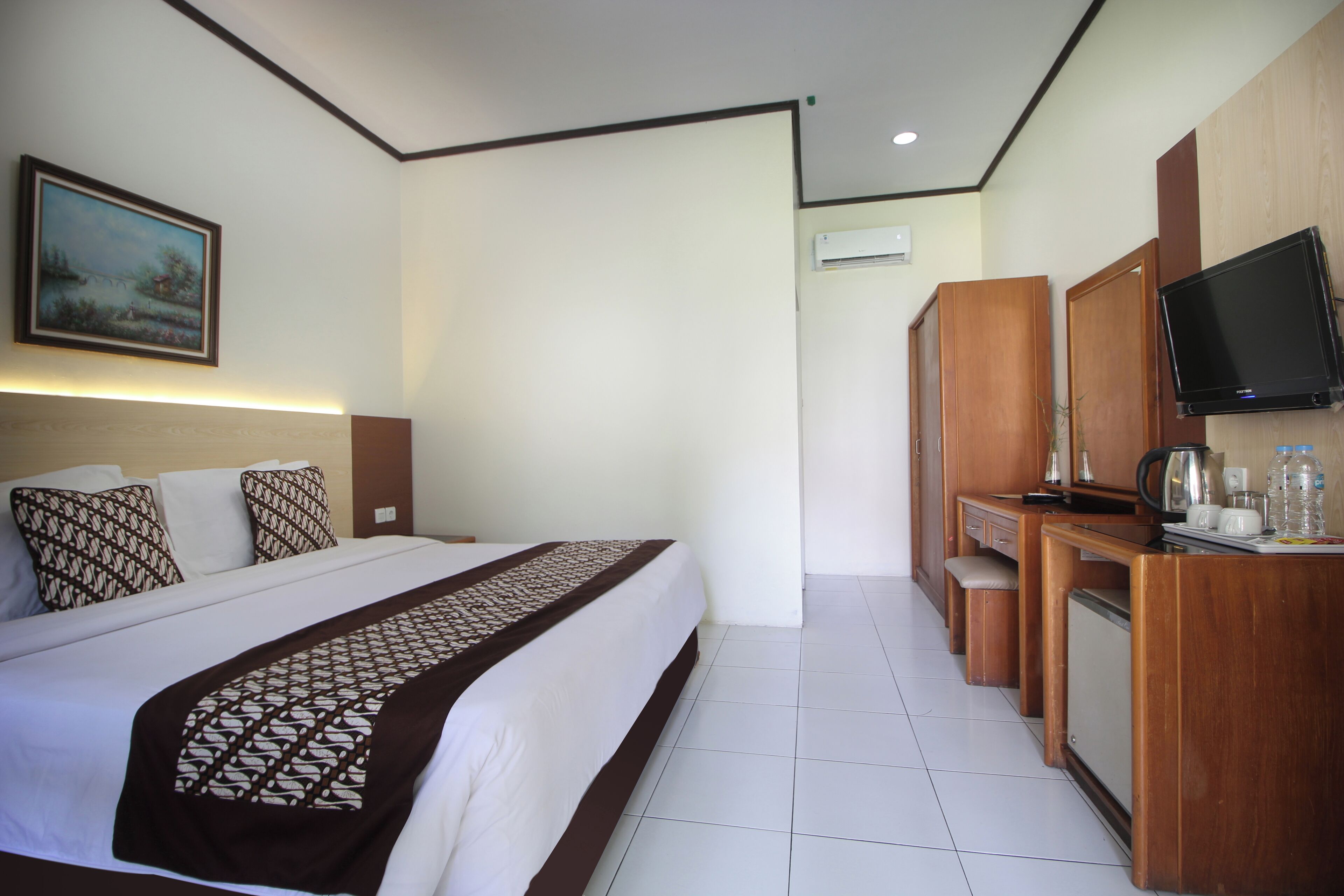 A hotel room with a bed, a desk with a television, and a painting on the wall.