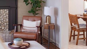 Una sala de estar moderna con un sofá, un sillón de cuero, una mesita de noche con una lámpara, una chimenea y un comedor con mesa y sillas.