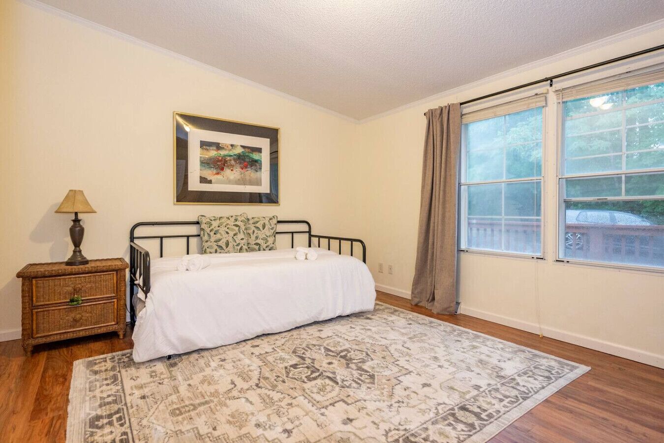 Quarto com cama, mesa de cabeceira, luminária, quadro na parede e janela com cortinas.
