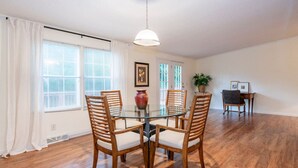 A dining area with a glass table surrounded by wooden chairs, a vase, and a hanging light fixture.