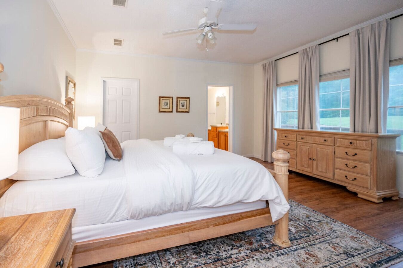 A bedroom with a large bed, wooden headboard, a dresser, and a ceiling fan.