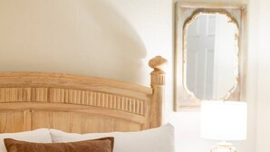 A neatly made bed with white linens, a brown pillow, and rolled towels on a wooden headboard.