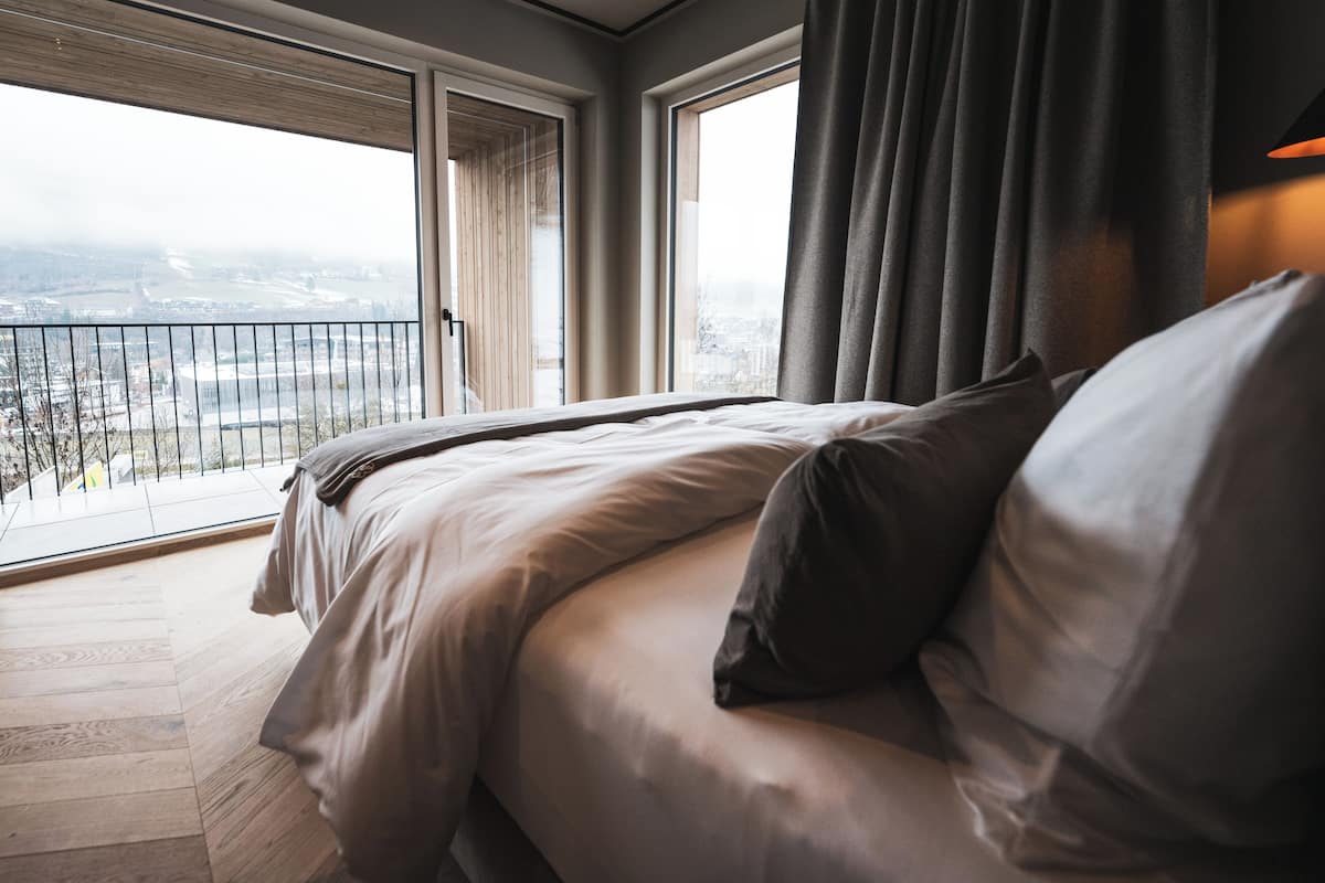 Une chambre avec un grand lit, une vue sur la ville depuis un balcon, et une fenêtre avec des rideaux.