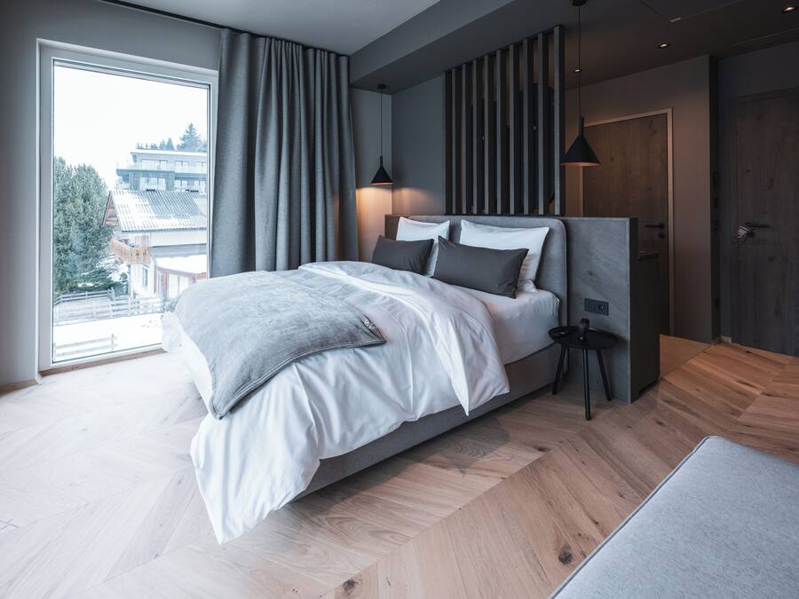 Un dormitorio moderno con una cama grande, una mesita pequeña y vistas a un edificio a través de una ventana.