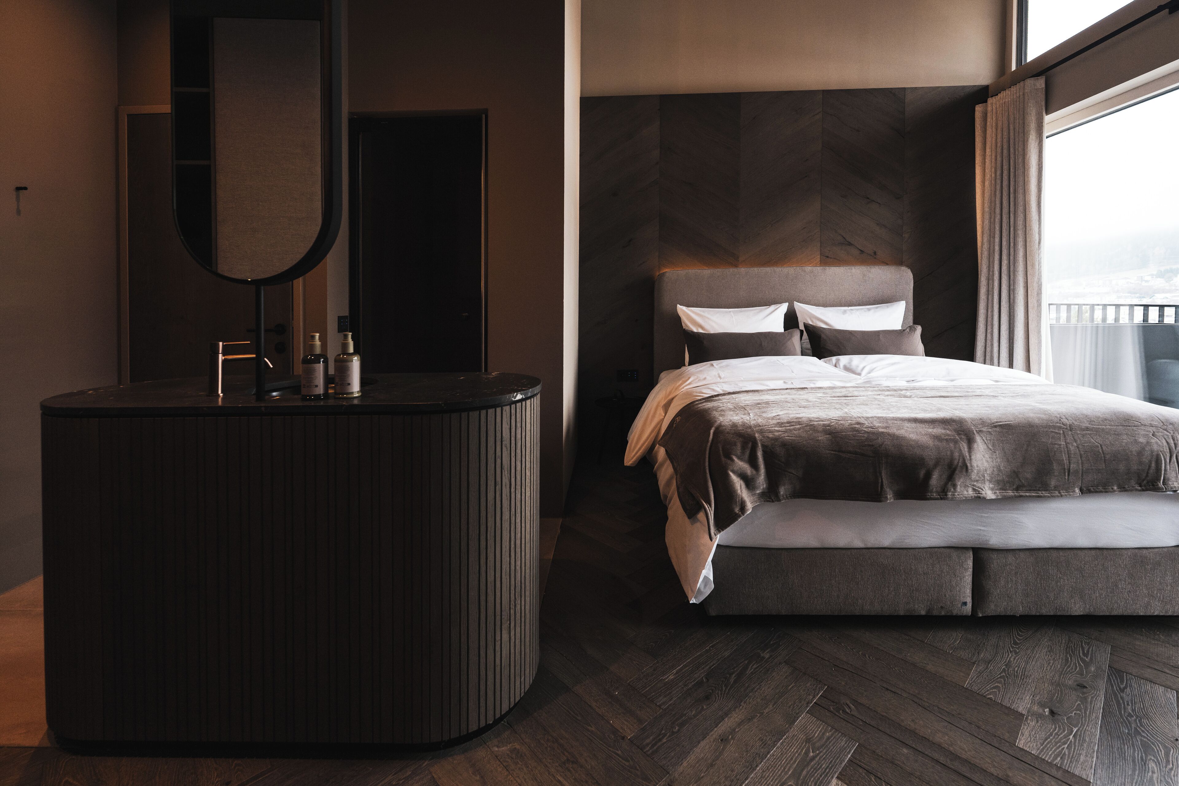 Une chambre à coucher moderne, dotée d’un grand lit, d’une coiffeuse avec un miroir et offrant une vue sur la ville grâce à une grande fenêtre.