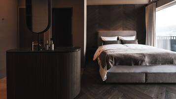 A modern bedroom with a large bed, a vanity with a mirror, and a view of the city through a large window.