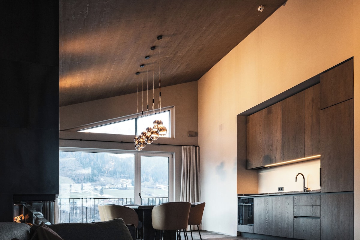 Une cuisine moderne avec des meubles en bois, un coin repas comprenant un canapé et des chaises, et une vue sur un paysage enneigé par de grandes fenêtres.