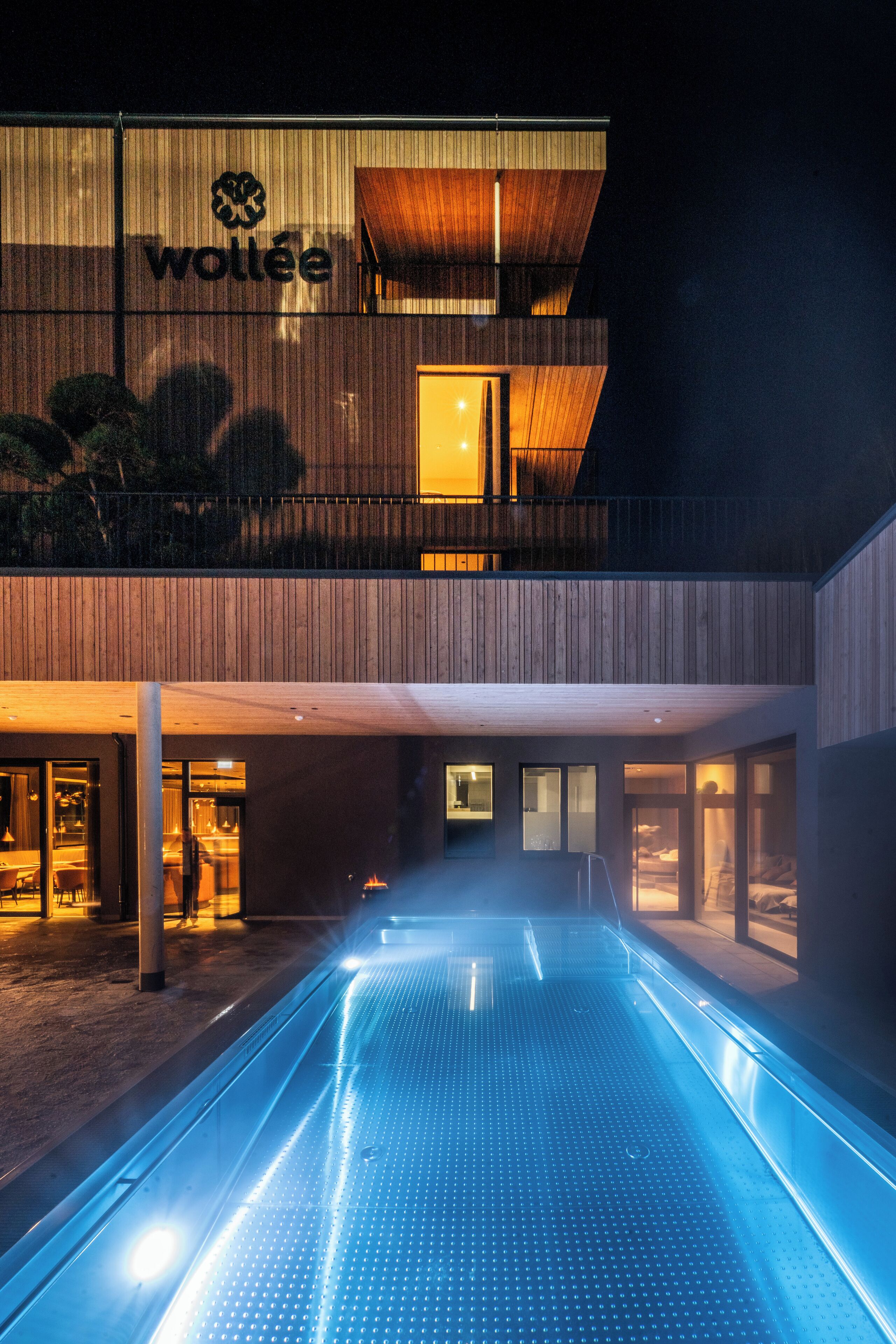 A modern hotel with a pool area, wooden exterior, and a visible sign reading "wollee".