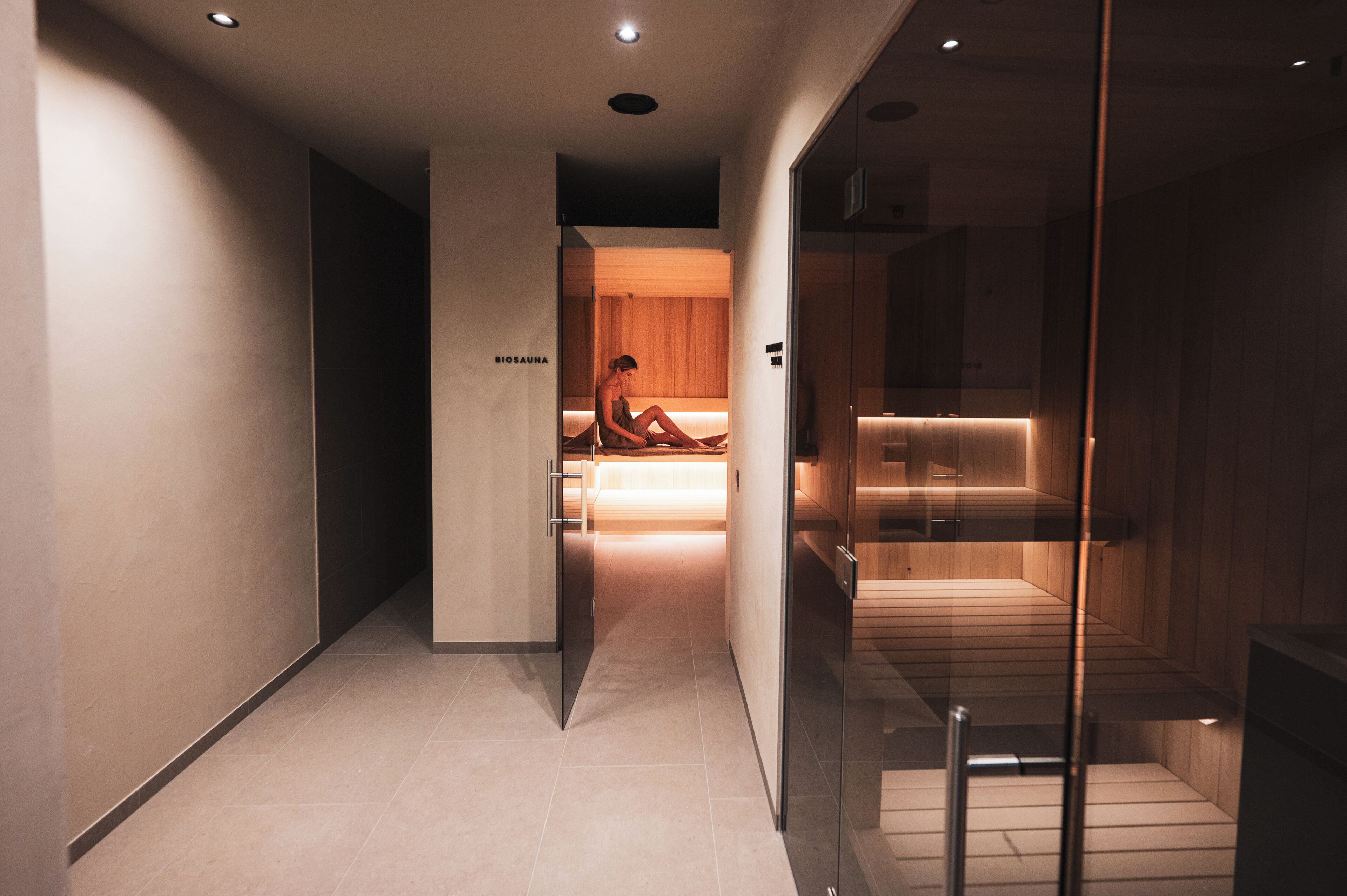 A modern hotel corridor with a visible spa area, a reception desk, and a glass partition.