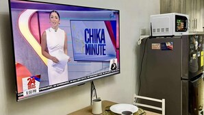 A kitchen with a TV displaying 'CHIKA MINUTE', a dining table set with plates and glasses, and a refrigerator with magnets. - Relaxing City Retreat (Mandaluyong City)