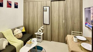 A modern living room with a sofa, a small dining table, a TV, and a wooden wardrobe. - Relaxing City Retreat (Mandaluyong City)