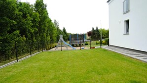 Eine Rasenfläche mit Spielplatz, einem weißen Gebäude und einem Zaun.