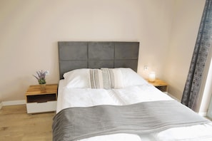 A neatly made bed with a grey headboard, a bedside table with a lamp, and a small plant. - Comfortable Holiday Home for 4 People (gmina Wolin)