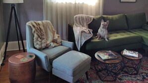 Een woonkamer met een groene bank, een lichtblauwe fauteuil, een klein rond tafeltje en een vloerlamp.