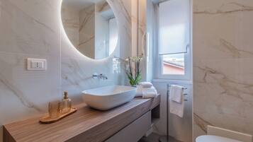 Un baño moderno con tocador de mármol, un espejo redondo grande, un lavabo sobre encimera y un perchero para toallas.