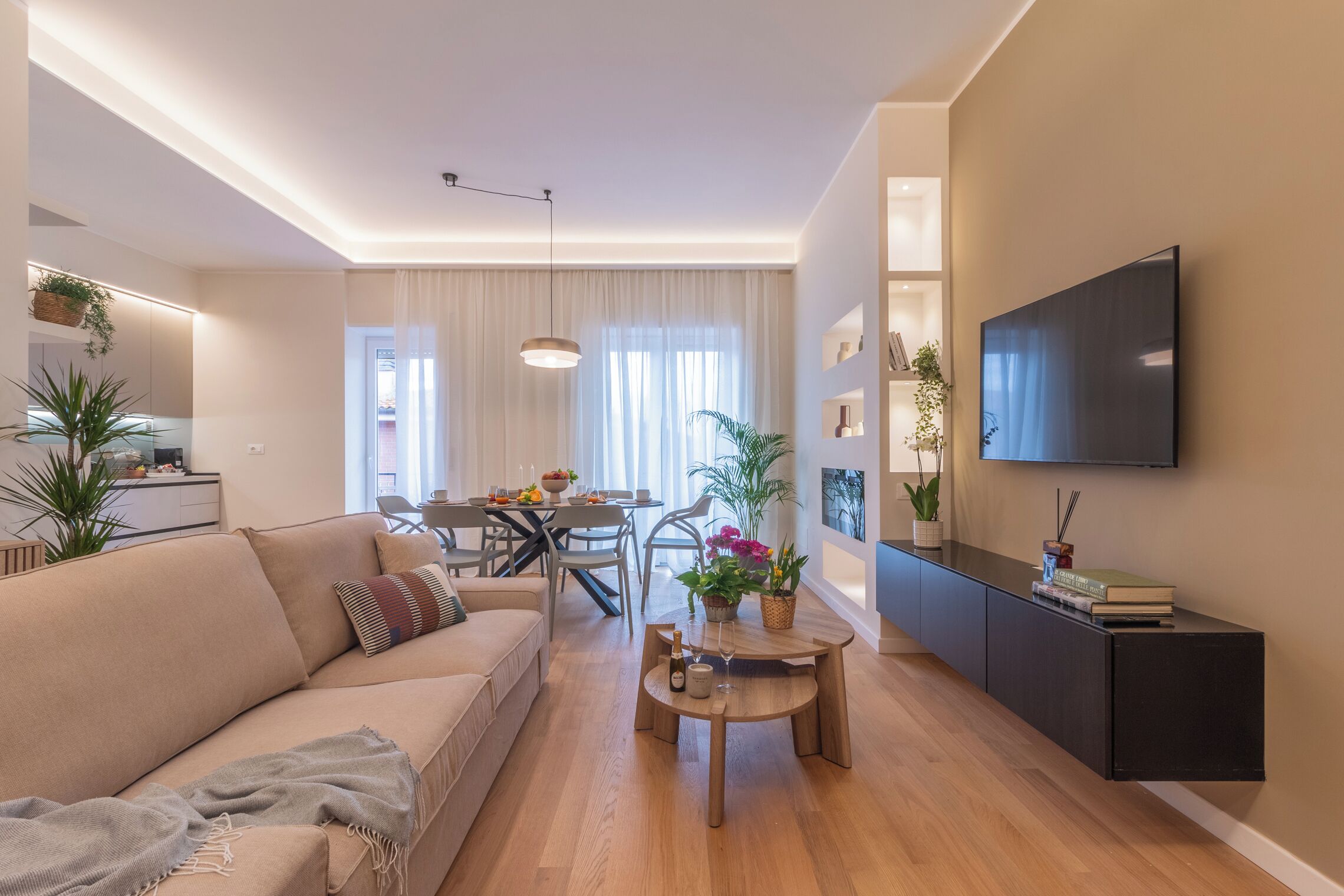 Ein modernes Wohnzimmer mit einer Couch, einem Esstisch und einem an der Wand befestigten Fernseher.