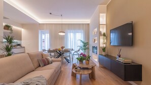A modern living room with a sofa, dining table, and a TV mounted on the wall.