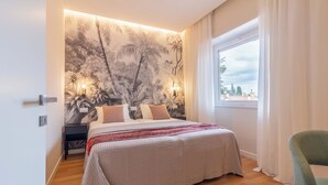 A bedroom with a large bed, a nightstand, a green chair, and a window with curtains.